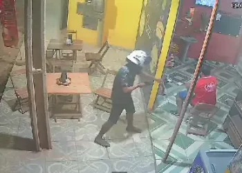 Dois homens chegam em uma motocicleta. O ocupante da garupa desce, já com a arma em punho, e vai em direção ao comerciante. (Reprodução/ Redes sociais)