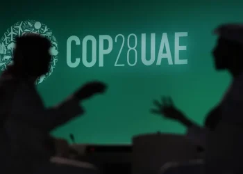 Silhueta de duas pessoas perto de um painel com o logo da COP 28 exibido em Dubai. — Foto: AP Photo/Rafiq Maqbool