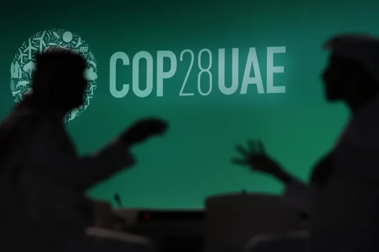 Silhueta de duas pessoas perto de um painel com o logo da COP 28 exibido em Dubai. — Foto: AP Photo/Rafiq Maqbool