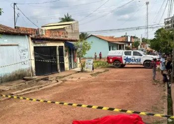 A imagem mostra moradores no local do crime, que está isolado, e o corpo da vítima coberto por um lençol vermelho.