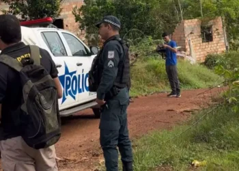 A imagem em destaque mostra um policial militar, uma viatura da corporação e outras pessoas onde o crime ocorreu. (Foto: Reprodução | Portal Giro)